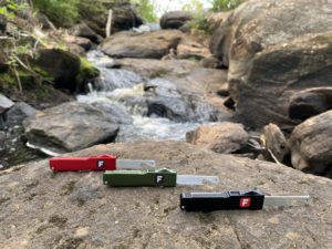 The Out the Front Bottle Opener by Flipped Tools comes in three distinguished colors. All three are lined up on top of a large rock, in the outdoors somewhere.