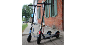 Two H300 Electric Folding Kick Scooters from Huffy Bikes side by side by a brick wall.