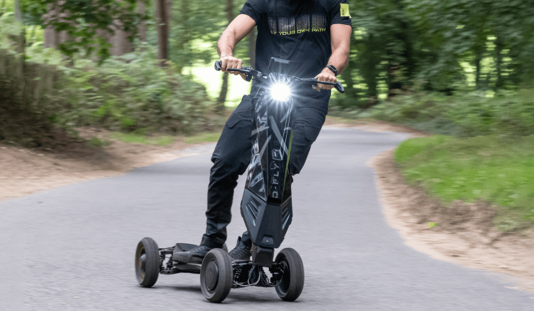 A man rides an electric scooter like no other, the dragonfly hyperscooter, on a paved path surrounded by green scenery. The background is blurred because of how fast the man on the electric scooter is going. The dragonfly hyperscooter is just one of a handful of the best electric scooters to buy.