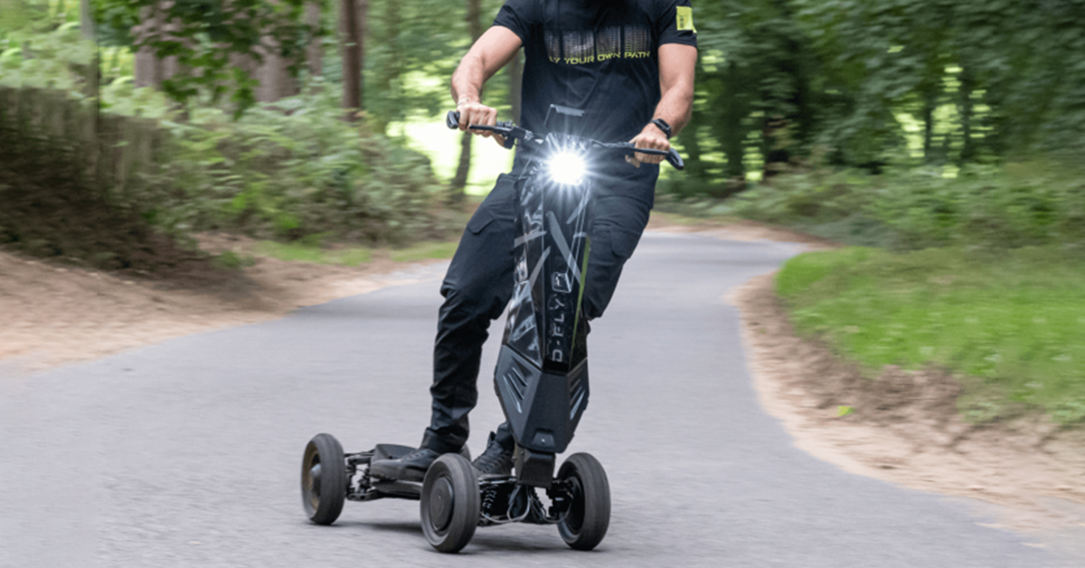 A man rides an electric scooter like no other, the dragonfly hyperscooter, on a paved path surrounded by green scenery. The background is blurred because of how fast the man on the electric scooter is going. The dragonfly hyperscooter is just one of a handful of the best electric scooters to buy.